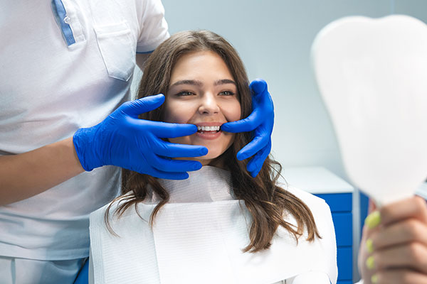 The image depicts a woman in a dental chair receiving care from a dental professional, with visible dental equipment and the professional wearing protective gloves.