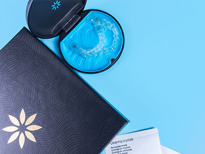 The image shows a black box with a blue and white patterned cover, placed on a surface next to a toothbrush in its case.