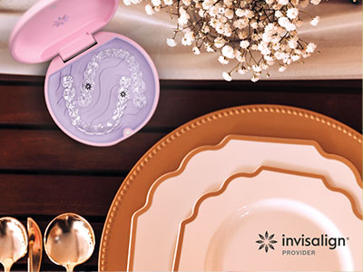An advertisement with a table setting featuring various plates, a box of dental floss, and a spoon, all arranged on a wooden surface with a pink lid in the foreground.