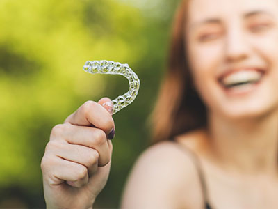 A young woman is holding a clear retainer in her hand, smiling and enjoying the moment.