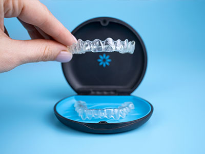 A person s hand holding a clear plastic tray with a blue dental impression kit, showcasing the components of the kit.