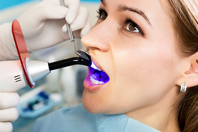 A woman receiving a dental cleaning, with a dental hygienist using a specialized device to clean her teeth.