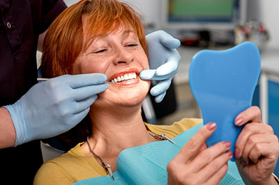 A woman is seated in a dental chair, receiving dental care with a smile on her face.