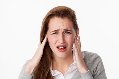 A woman with a concerned expression, hand on her head, appearing to be experiencing discomfort or pain.