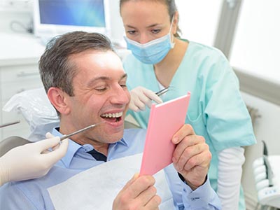 A man in a dental chair, holding a pink card with a smile, while a dentist and hygienist look on.