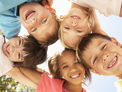 A group of children smiling at the camera in a sunny outdoor setting.