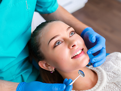 The image shows a dental professional performing a cosmetic procedure on a patient, with the patient smiling and looking towards the camera.