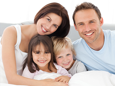 A family of four, including a man, woman, and two children, posing for a photo in bed.