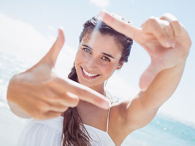 The image shows a woman taking a selfie with her hand, smiling and looking directly at the camera.