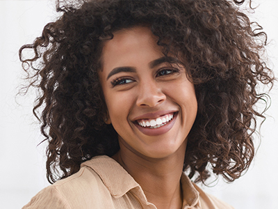 The image shows a smiling individual with curly hair, wearing a light-colored top.